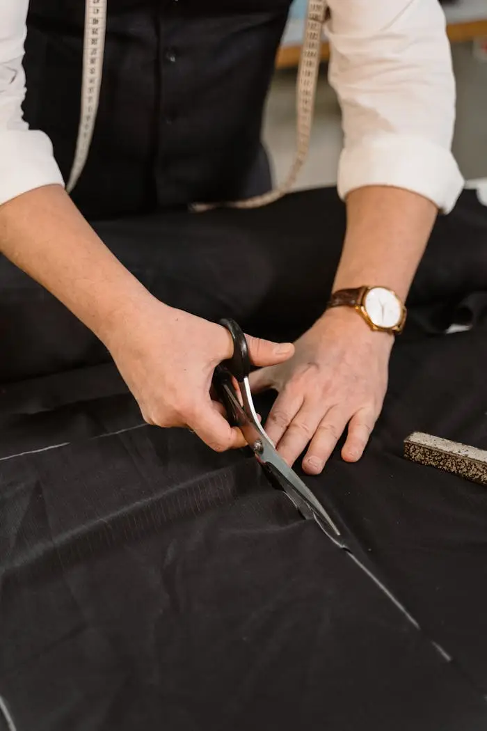 Close-up of a professional tailor carefully cutting black fabric in a workshop.